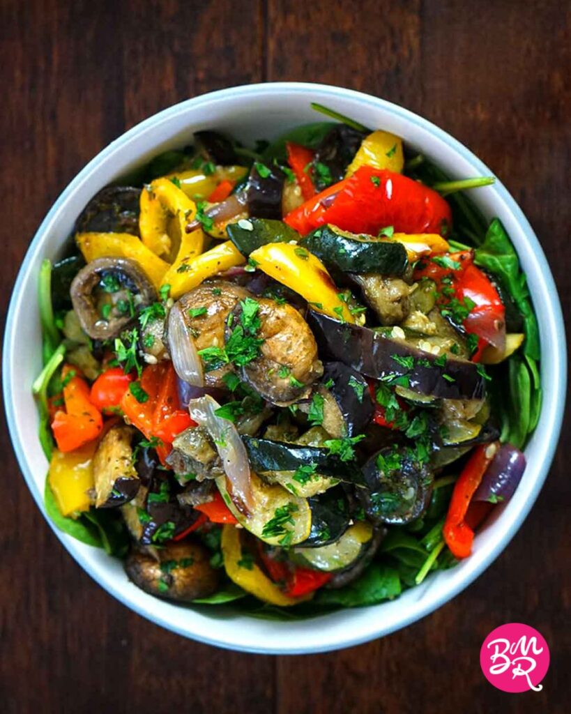 top down view of a roasted vegetable salad in a light blue bowl on a dark wooden table