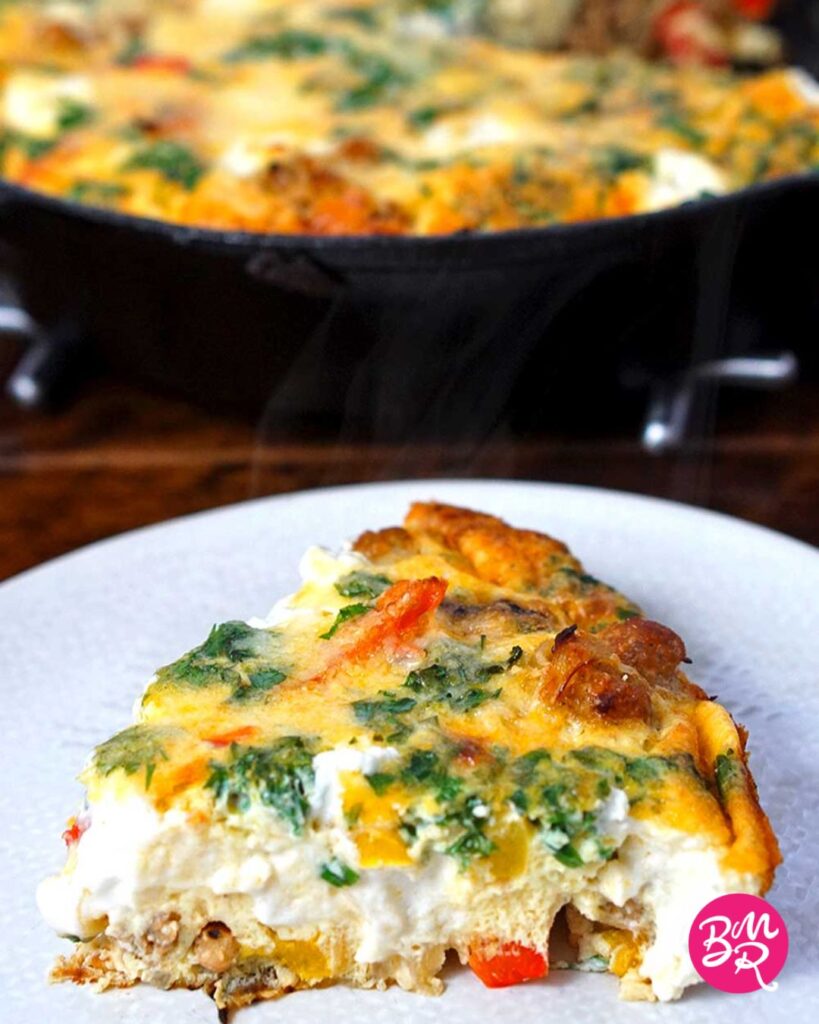 slice of sausage frittata on a white plate placed in front of a cast iron pan with the rest of the frittata blurred in the background